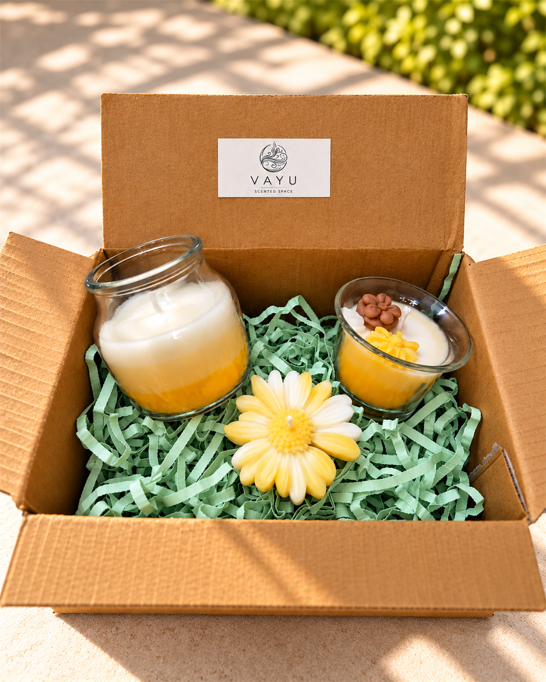 Two layered yellow and white glass jar candles and a cream daisy candle in a Vayu hamper box