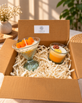 Two decorative yellow and white candles in clear glass vessels inside a Vayu gift box