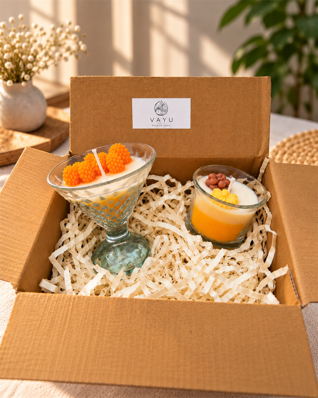 Two decorative yellow and white candles in clear glass vessels inside a Vayu gift box