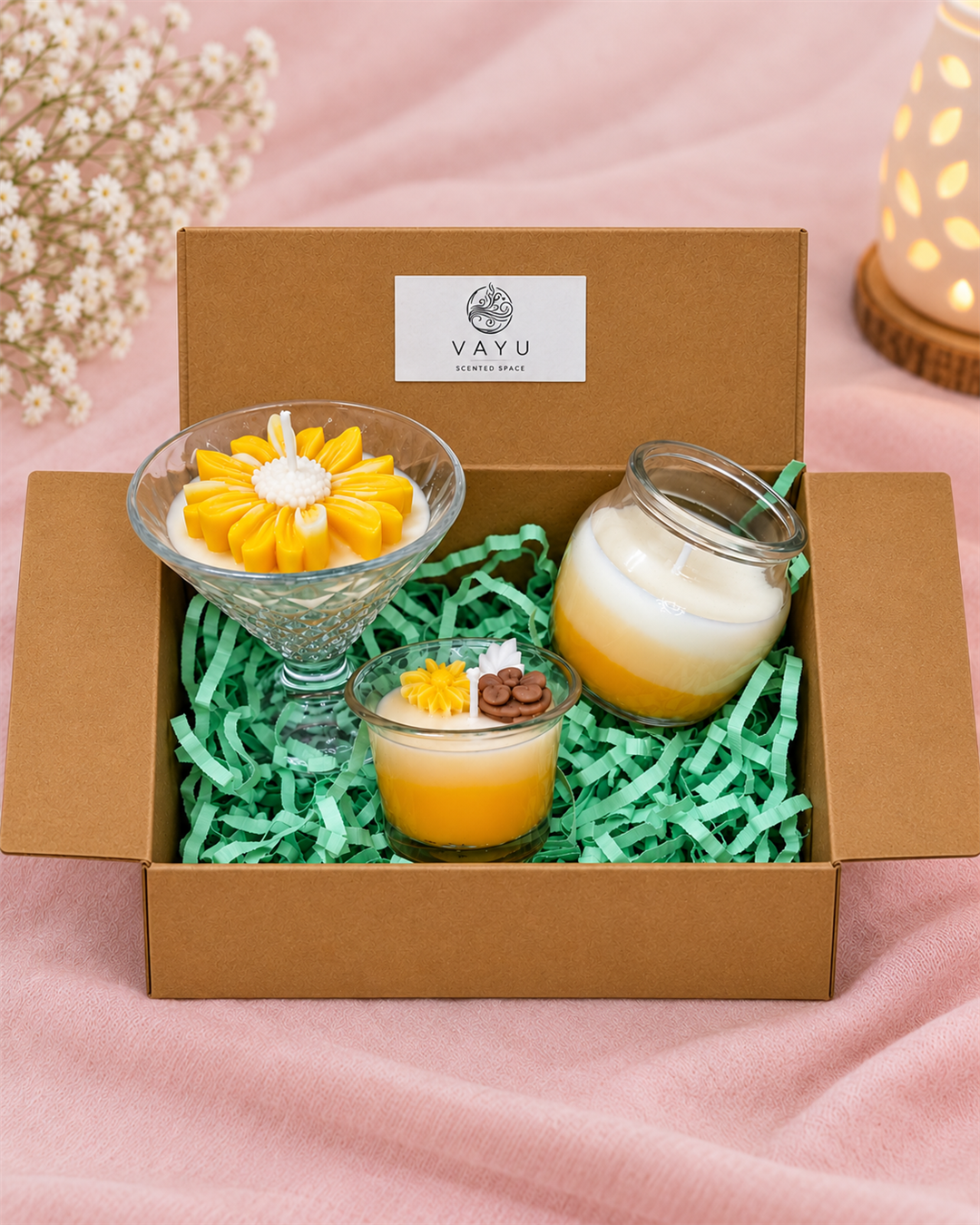 Three yellow and white candles in a crystal-cut stemmed glass, curved jar, and floral tumbler in a Vayu gift box